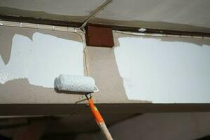 de cerca un pintado rodillo es pintado blanco en el pared de antiguo casa. foto