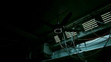 A dark concrete interior with a ceiling fan and multiple wires hanging from it photo