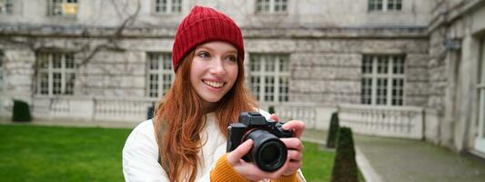 Happy redhead girl tourist, takes photos, photographer with professional camera walks around city and captures beautiful pictures photo