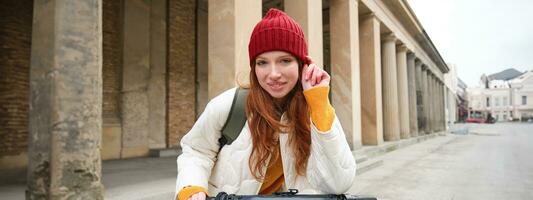 Smiling redhead european girl drives public escooter, tourist explores city, rides in city centre photo