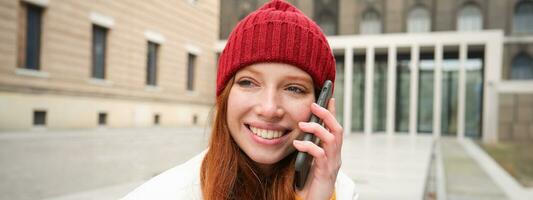 Mobile connection and people concept. Happy redhead woman in hat, talks on mobile phone, making telephone call, using app to call abroad photo