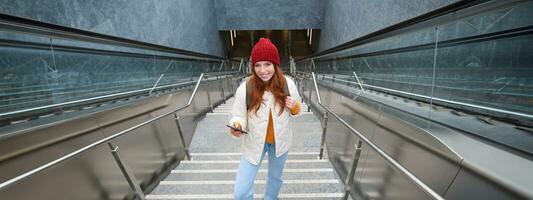 Outdoor shot of young woman plans route, follows map on smartphone app, goes up stairs with backpack and smiles photo