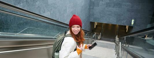 Smiling girl walking on stairs, using mobile phone, texting message on her way, using smartphone app map, follows route to destination place photo