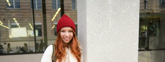 Beautiful redhead girl with smartphone, standing on street, holding mobile phone, using taxi app, connects to public wifi and uses internet, sends a text message photo