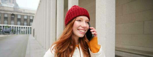 Happy redhead woman, girl with phone talks, has conversation on mobile app, uses internet to call abroad with smartphone app, laughing and smiling photo