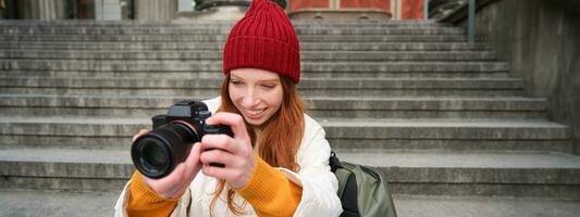 retrato de joven fotógrafo chica, se sienta en escalera con profesional cámara, toma fotos al aire libre, haciendo estilo de vida disparo