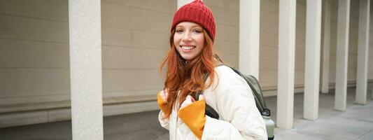 Female tourist in red hat with backpack, sightseeing, explores historical landmarks on her trip around europe, smiling and posing on street photo