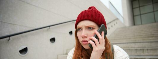 Redhead girl with concerned face, looking worried while answering phone call, hears bad news over telephone conversation, rings someone with upset emotion photo