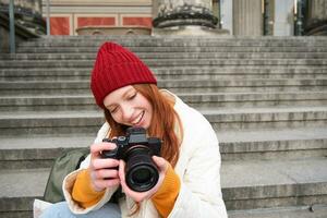 Portrait of young photographer girl, sits on stairs with professional camera, takes photos outdoors, making lifestyle shooting