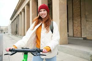 Smiling redhead european girl drives public escooter, tourist explores city, rides in city centre photo