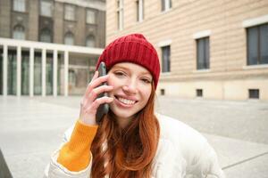 Mobile connection and people concept. Happy redhead woman in hat, talks on mobile phone, making telephone call, using app to call abroad photo