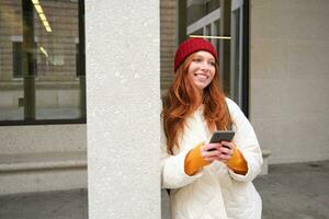 Stylish urban girl using mobile phone app, standing in city, waiting for taxi, looking at smartphone application, texting message photo
