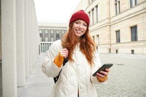 Beautiful smiling girl, tourist with backpack, holding smartphone, using map on mobile phone application, looking for sightseeing in internet app, standing outdoors photo