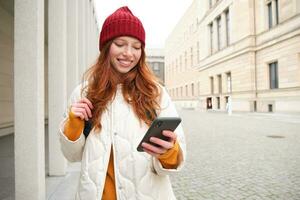 Beautiful smiling girl, tourist with backpack, holding smartphone, using map on mobile phone application, looking for sightseeing in internet app, standing outdoors photo