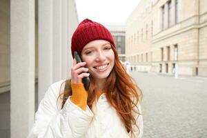 Happy redhead woman, girl with phone talks, has conversation on mobile app, uses internet to call abroad with smartphone app, laughing and smiling photo