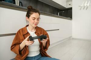 Portrait of attractive woman puts on wireless headphones, sits on floor, relaxing with favourite songs on playlist, enjoys listening to podcast photo