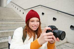 Urban people and lifestyle. Happy redhead woman takes photos, holding professional digital camera, photographing on streets photo