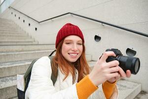 Portrait of female photographer walking around city with professional camera, taking pictures capturing urban shots, photographing outdoors photo