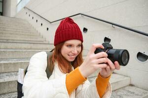 Urban people and lifestyle. Happy redhead woman takes photos, holding professional digital camera, photographing on streets photo