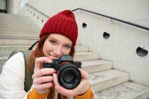 Portrait of female photographer walking around city with professional camera, taking pictures capturing urban shots, photographing outdoors photo