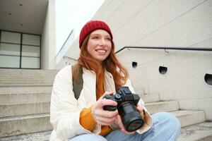 retrato de hembra fotógrafo caminando alrededor ciudad con profesional cámara, tomando imágenes capturar urbano tiros, fotografiando al aire libre foto