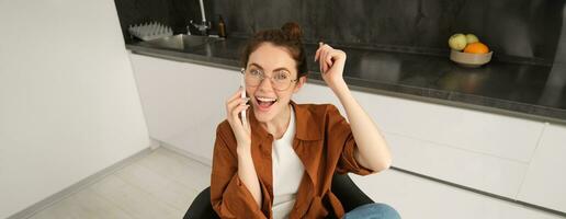 retrato de mujer recepción genial Noticias terminado el teléfono llamar, celebra y saltos en silla desde emoción durante teléfono conversacion foto