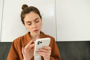 Close up portrait of woman looking at her smartphone with thoughtful face, online shopping, buying something on the internet using mobile app photo