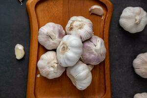 A large head of garlic lies on a wooden plate on a black background. photo
