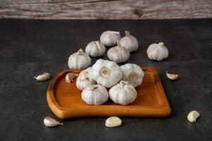 A large head of garlic lies on a wooden plate on a black background. photo