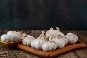 A large head of garlic lies on a wooden plate on a black background. photo