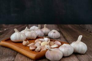 A large head of garlic lies on a wooden plate on a black background. photo