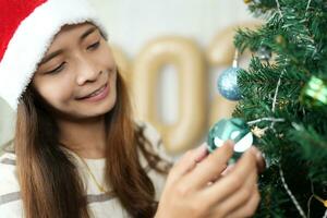 Merry Christmas 2024 concept Asian women decorate the Christmas tree with colorful Christmas balls. photo