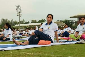 New Delhi, India, June 21, 2023 - Group Yoga exercise session for people at Yamuna Sports Complex in Delhi on International Yoga Day, Big group of adults attending yoga class in cricket stadium photo