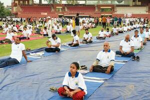 New Delhi, India, June 21, 2023 - Group Yoga exercise session for people at Yamuna Sports Complex in Delhi on International Yoga Day, Big group of adults attending yoga class in cricket stadium photo