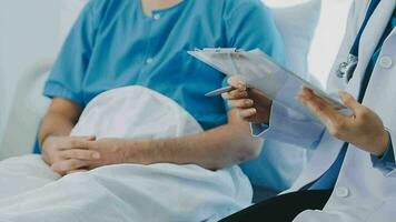 anziano medico e giovane maschio paziente chi menzogna su il letto mentre controllo polso, consultare e spiegare con infermiera assunzione Nota e supporto nel ospedale reparti. video