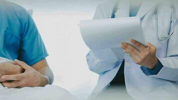 Senior doctor and young male patient who lie on the bed while checking pulse, consult and explain with nurse taking note and supporting in hospital wards. video