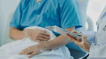 Senior doctor and young male patient who lie on the bed while checking pulse, consult and explain with nurse taking note and supporting in hospital wards. video