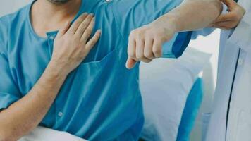 Senior doctor and young male patient who lie on the bed while checking pulse, consult and explain with nurse taking note and supporting in hospital wards. video