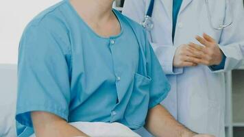 Senior doctor and young male patient who lie on the bed while checking pulse, consult and explain with nurse taking note and supporting in hospital wards. video