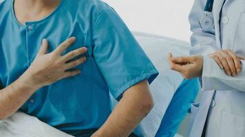 Senior doctor and young male patient who lie on the bed while checking pulse, consult and explain with nurse taking note and supporting in hospital wards. video