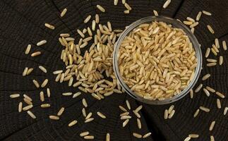 Bowl of brown rice groats on black wooden background. Top view photo