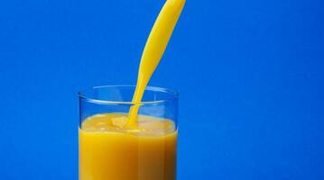 Orange juice pouring into glass, isolated on blue background photo