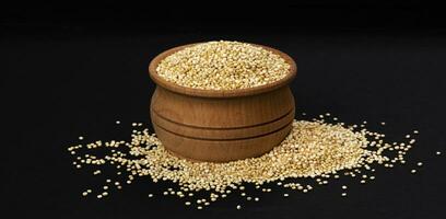Wooden bowl of quinoa seeds isolated on black background, close up photo