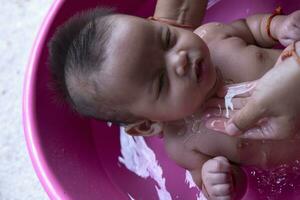 Calm Asian babe bathing in bathtub, having fun laughing Mother bathes daughter with warm water Relax and have a good time with mom. Concept of caring for newborns. photo