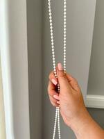 A female hand holding a beaded chain for the blinds photo