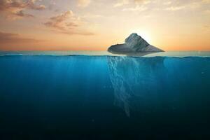 Ocean warming, concept. Iceberg in clear blue water and hidden danger under water at sunset. Iceberg - Hidden Danger And Global Warming Concept. Floating ice in ocean. Copy space for text and design. photo