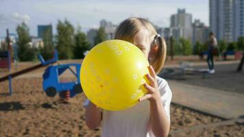 pequeno menina criança infla uma amarelo balão dentro a verão parque 4k video