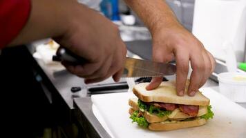 révélateur proche en haut coup de cuisinier mains Coupe une sandwich dans quatre les pièces à servir il à le clients video