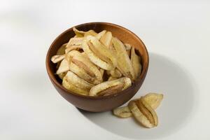 Banana chips in a wooden bowl on a white table photo