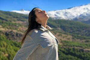 beautiful middle-aged latina woman, arms stretched back, breathing deeply, with the sun in front of her, high in the peaks of sierra nevada, granada. photo